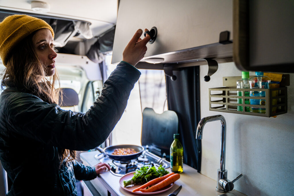 a woman getting something from an RV cabinet while cooking