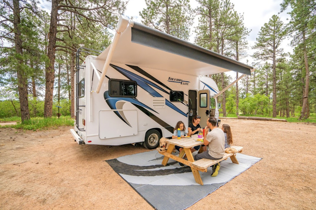a Class C camper set up in front of a picnic table