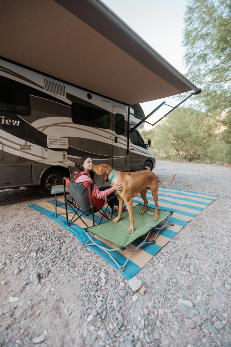 a woman in front of her shaded RV with her dog