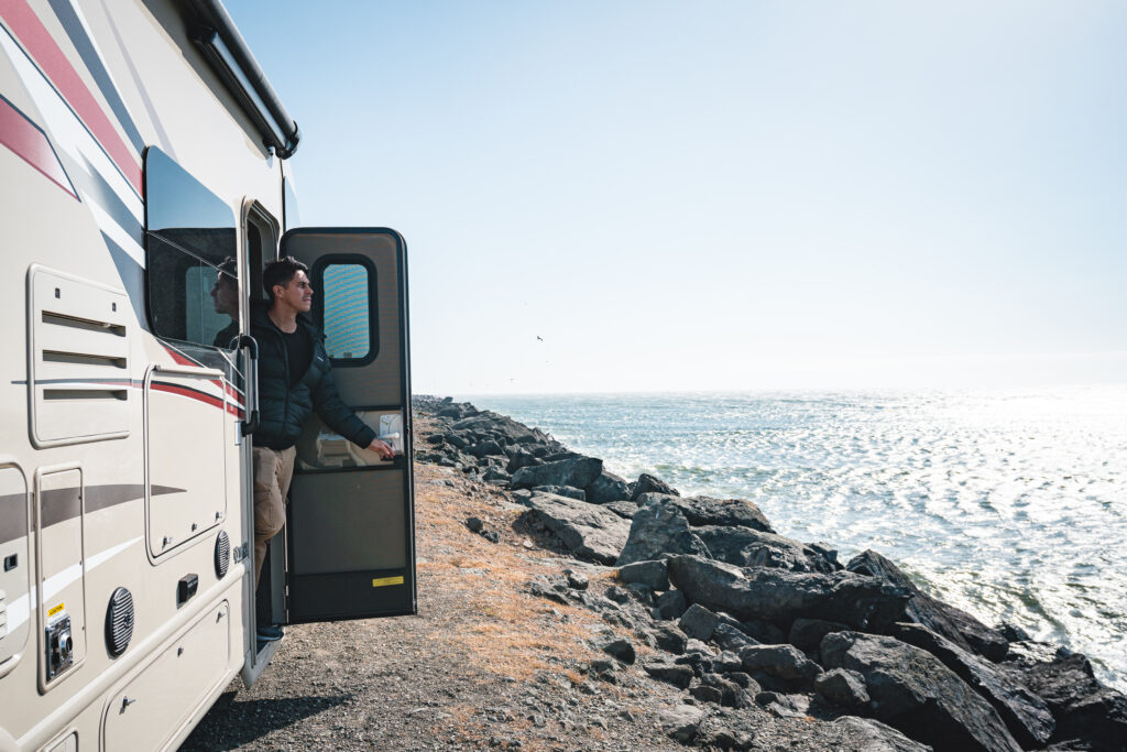 A man opening an RV door to a view of the ocean
