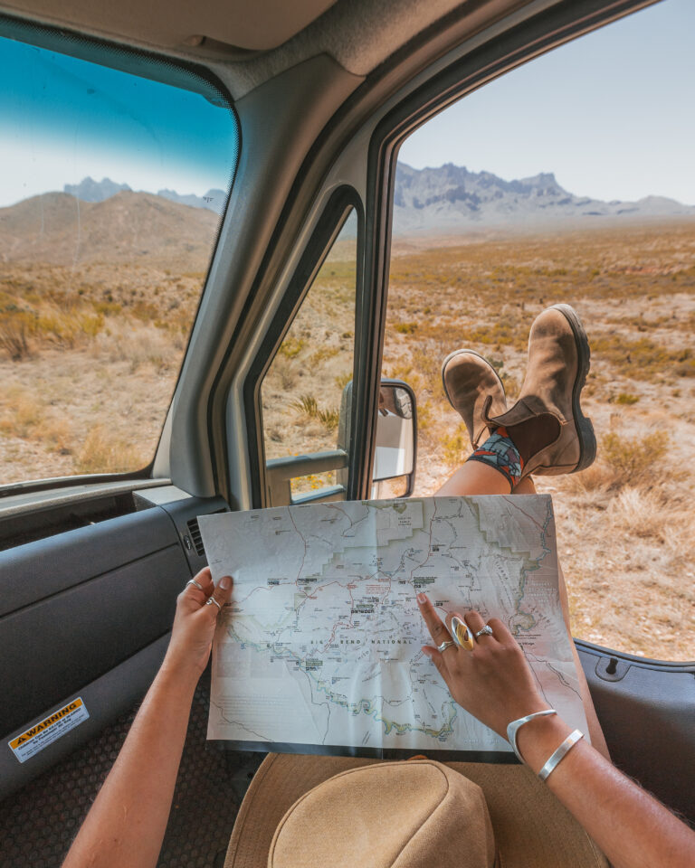 A woman looking at a map while relaxing in the front seat of a camper