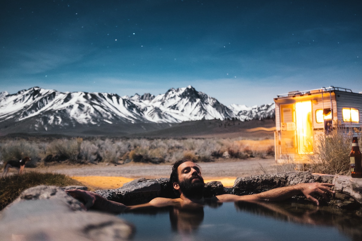 person in hot spring with RV and mountains behind them