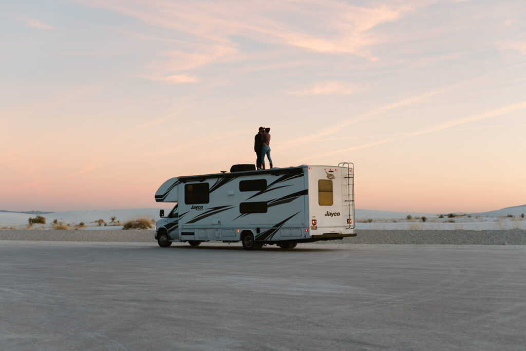 two people standing on top of their RV in the desert