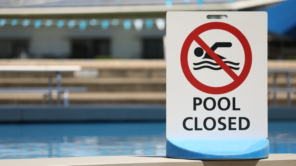 A pool closed sign with an empty pool behind