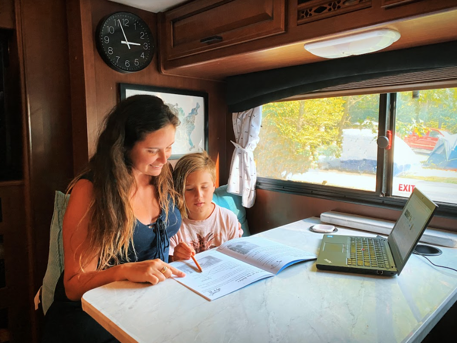 a woman and child doing schoolwork at an RV table