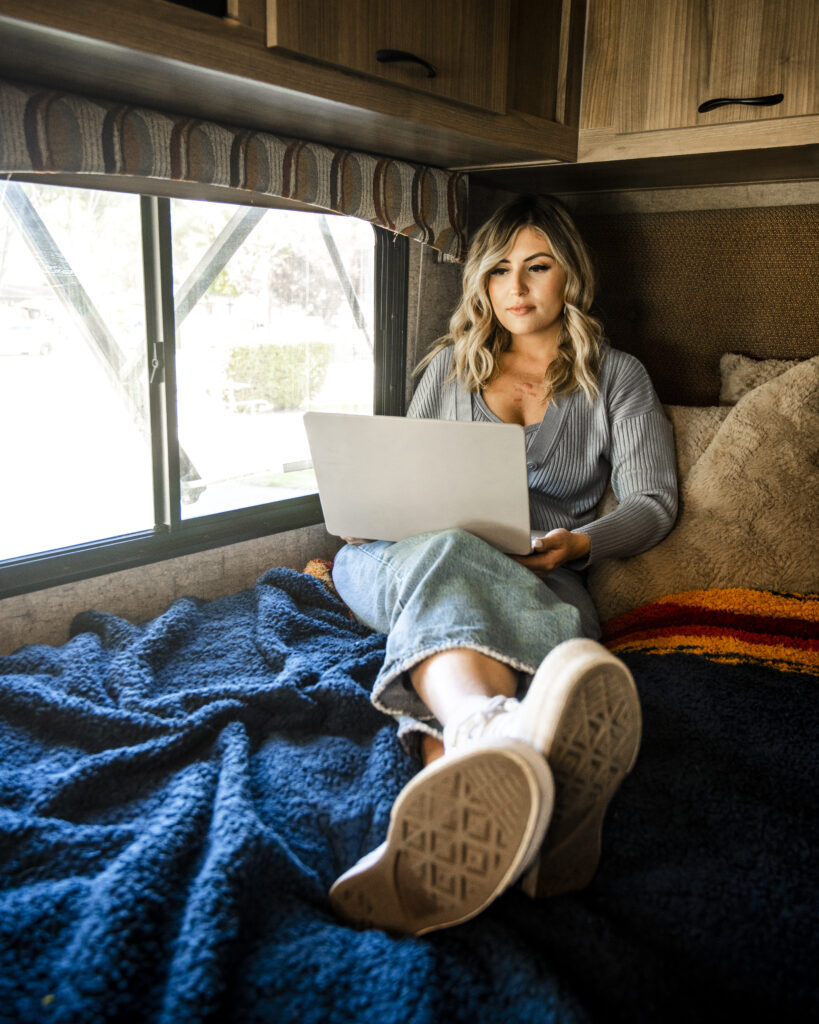 a woman relaxing on an RV bed working on a computer