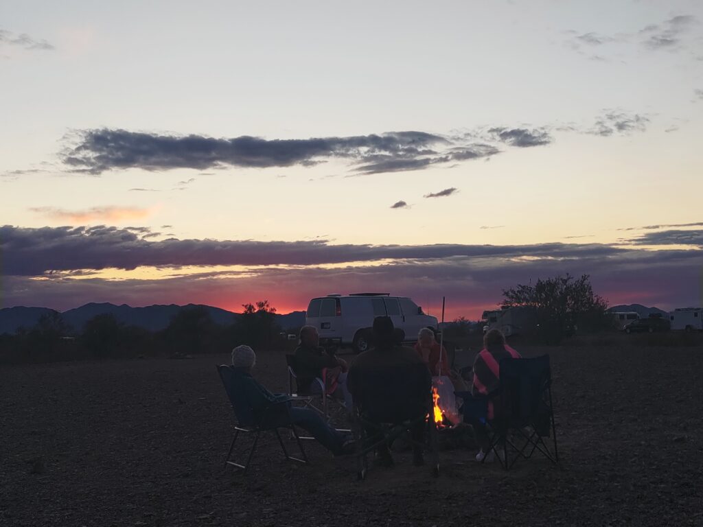 Group of friends gathers around a campfire at sunset