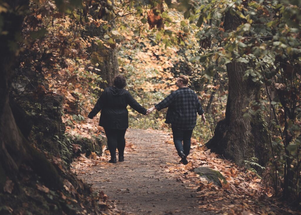 Couple holds hands while walking down the middle of a trail, surrounded by fall foliage