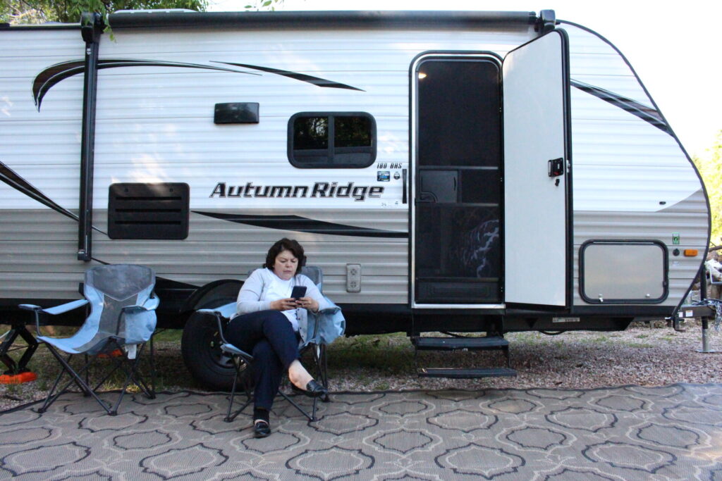 woman sitting outside travel trailer in her phone